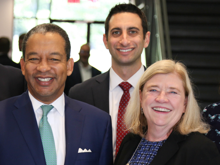 Two males and one female woman dressed in suits and ties smiling at the camera